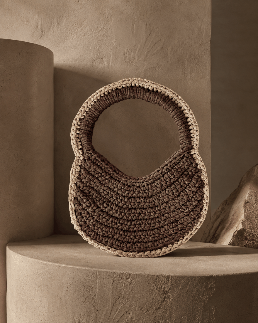 Bolsa Ojos de la Tierra · pieza marrón escultural sobre pedestal terracota · TUÁ